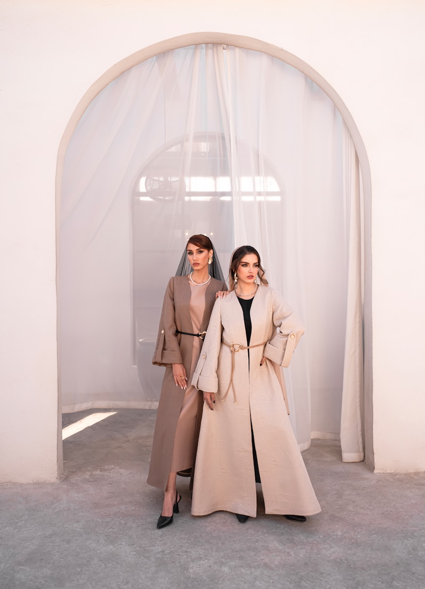 Two women in elegant abayas standing indoors.